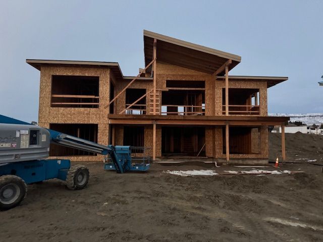 House under construction with exposed wood frame and unfinished siding; a lift is parked in front.