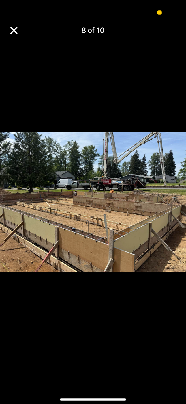 Construction site with foundation forms in foreground and concrete pump truck in the distance.