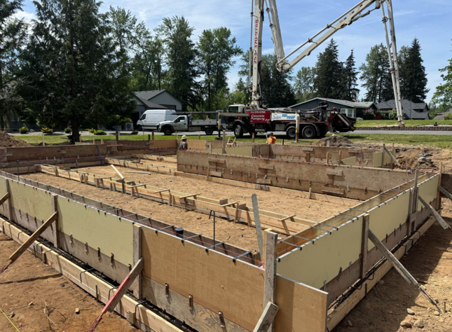 Construction site with concrete forms and a pump truck pouring concrete.