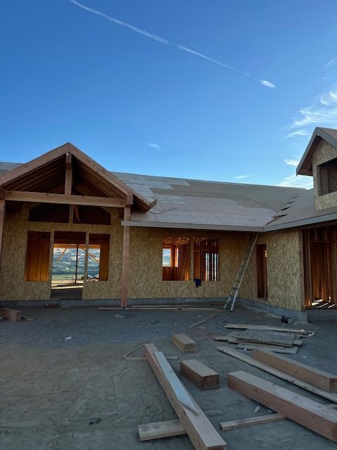 House under construction, wooden frame against a blue sky. Lumber and materials scattered on the concrete foundation.