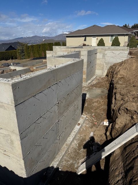 Concrete foundation walls in a construction site, next to a dirt embankment.