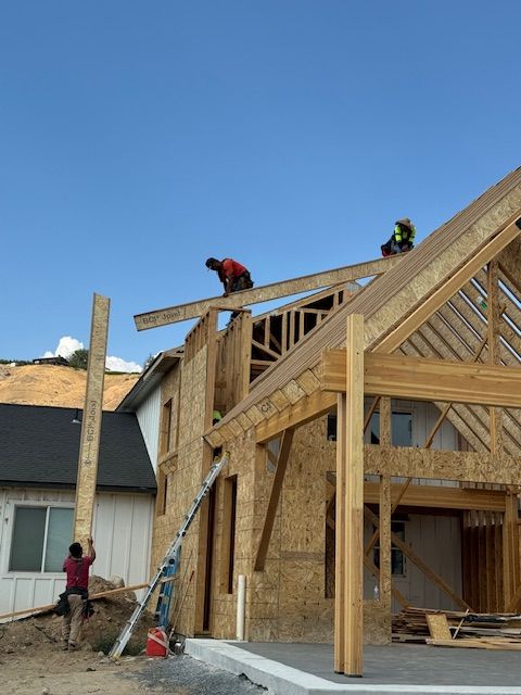 Construction workers building a house, using wooden beams and framing under a clear blue sky.
