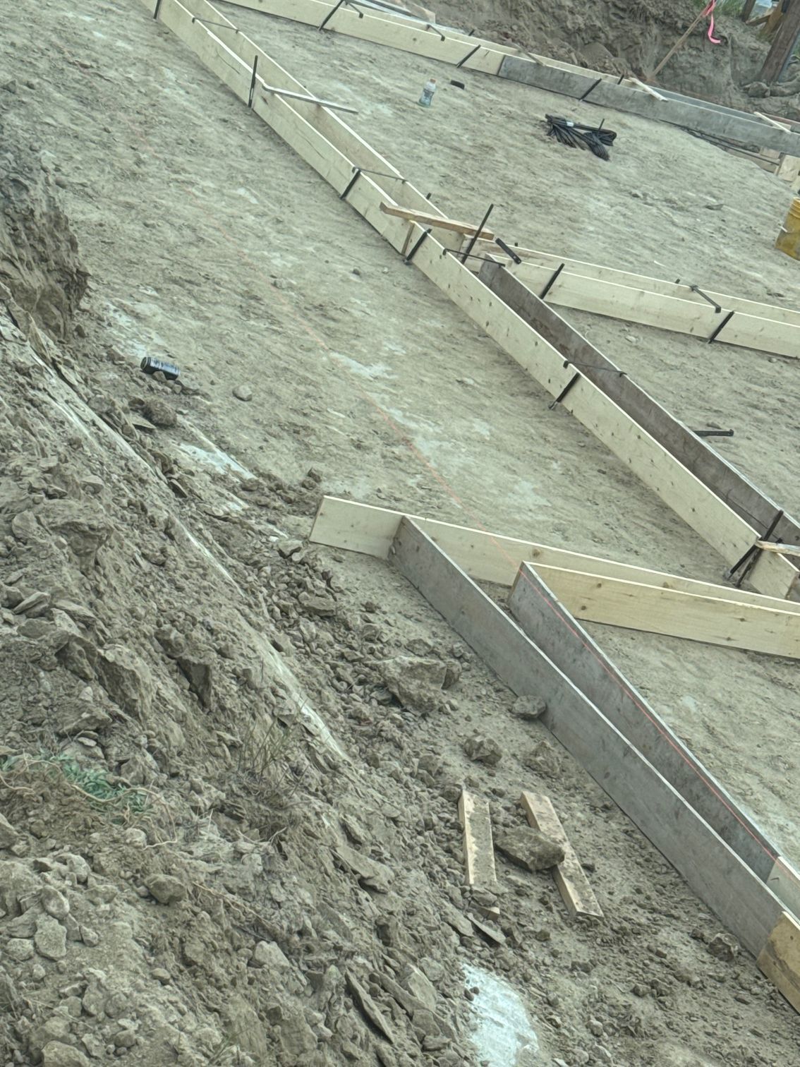 Wooden forms on a sloped, muddy construction site, ready for concrete.