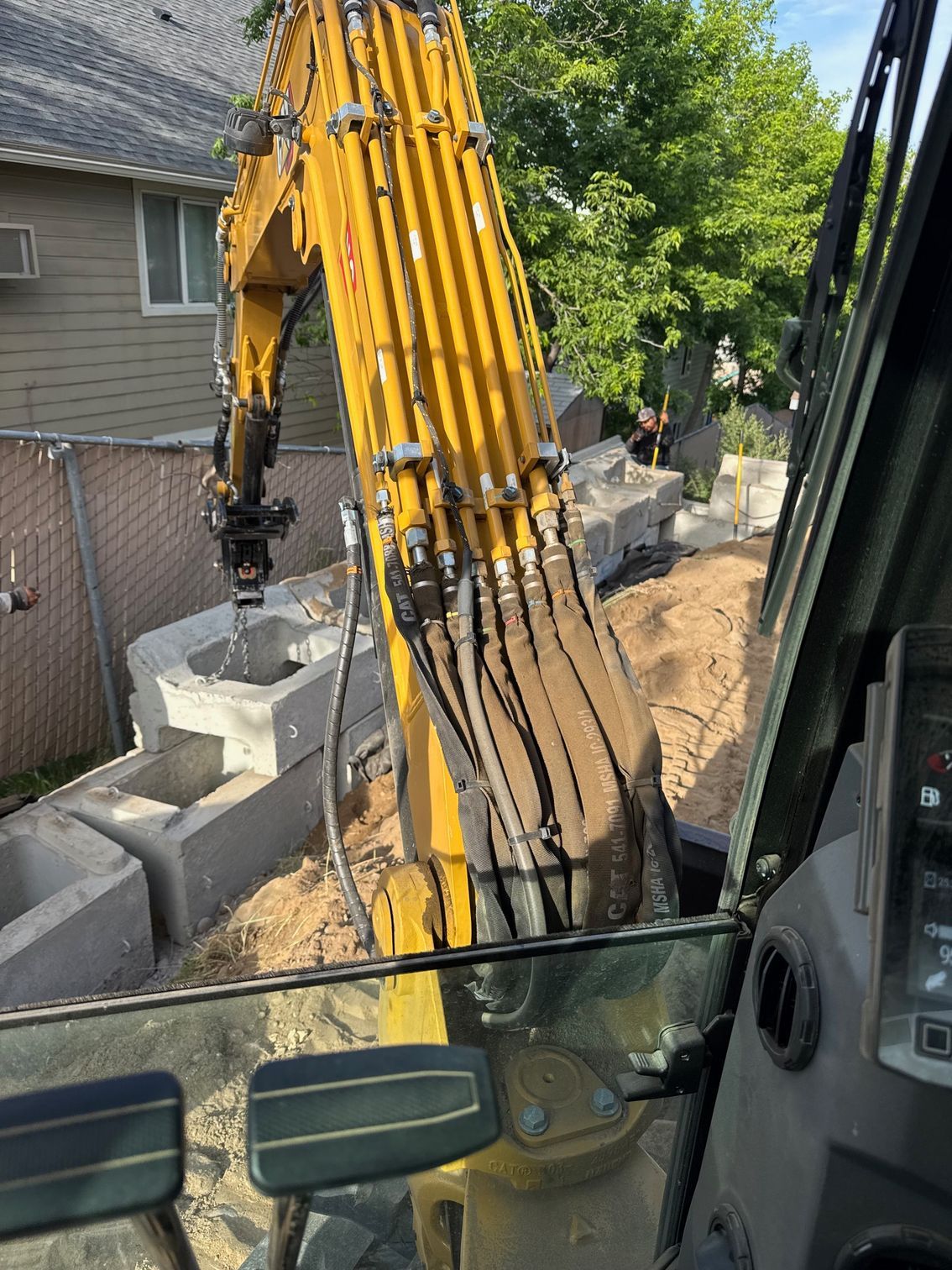 Yellow excavator moving concrete blocks near a fence and a house.
