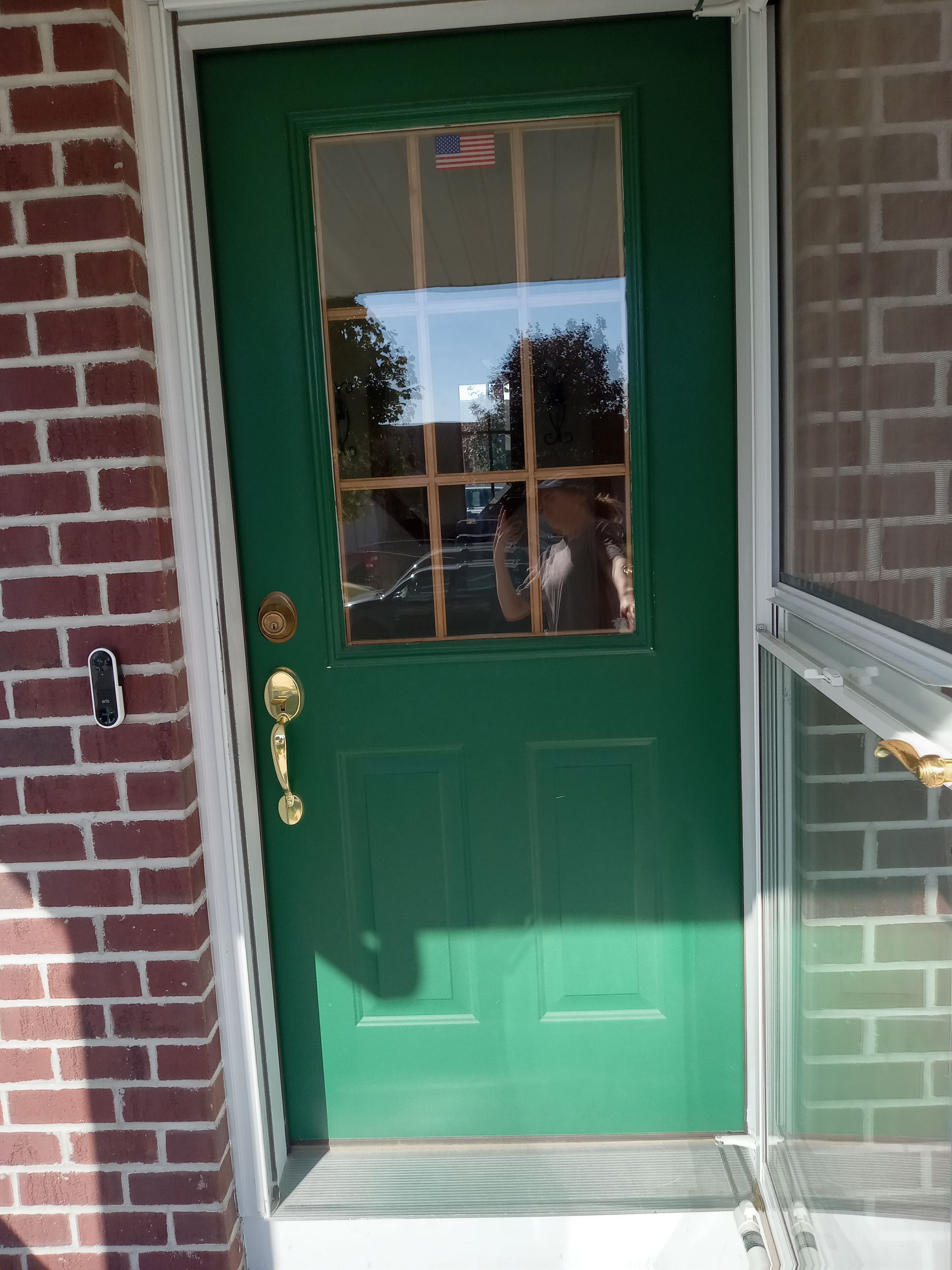 A green door with a window is on a brick building.