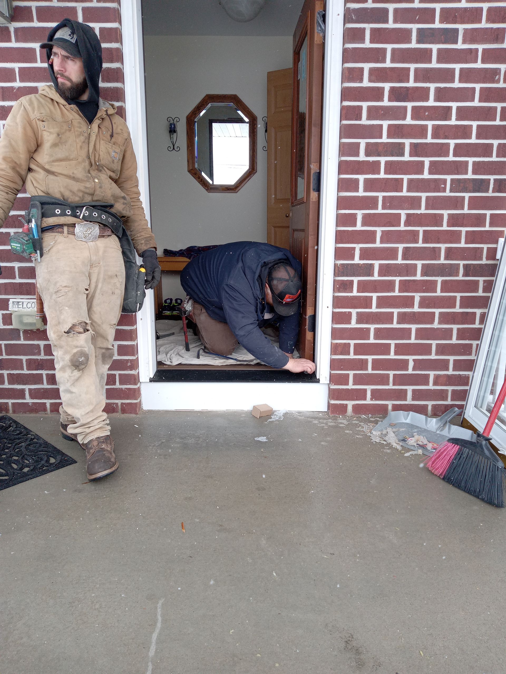 Two men are working on a door in a brick house.