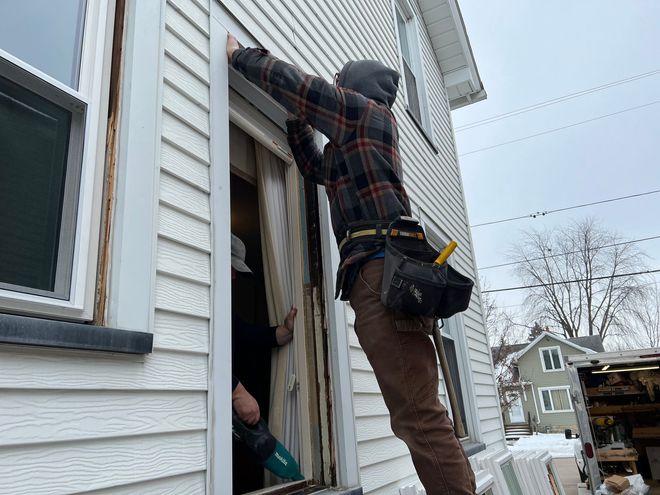 A man is working on a window on the side of a house.