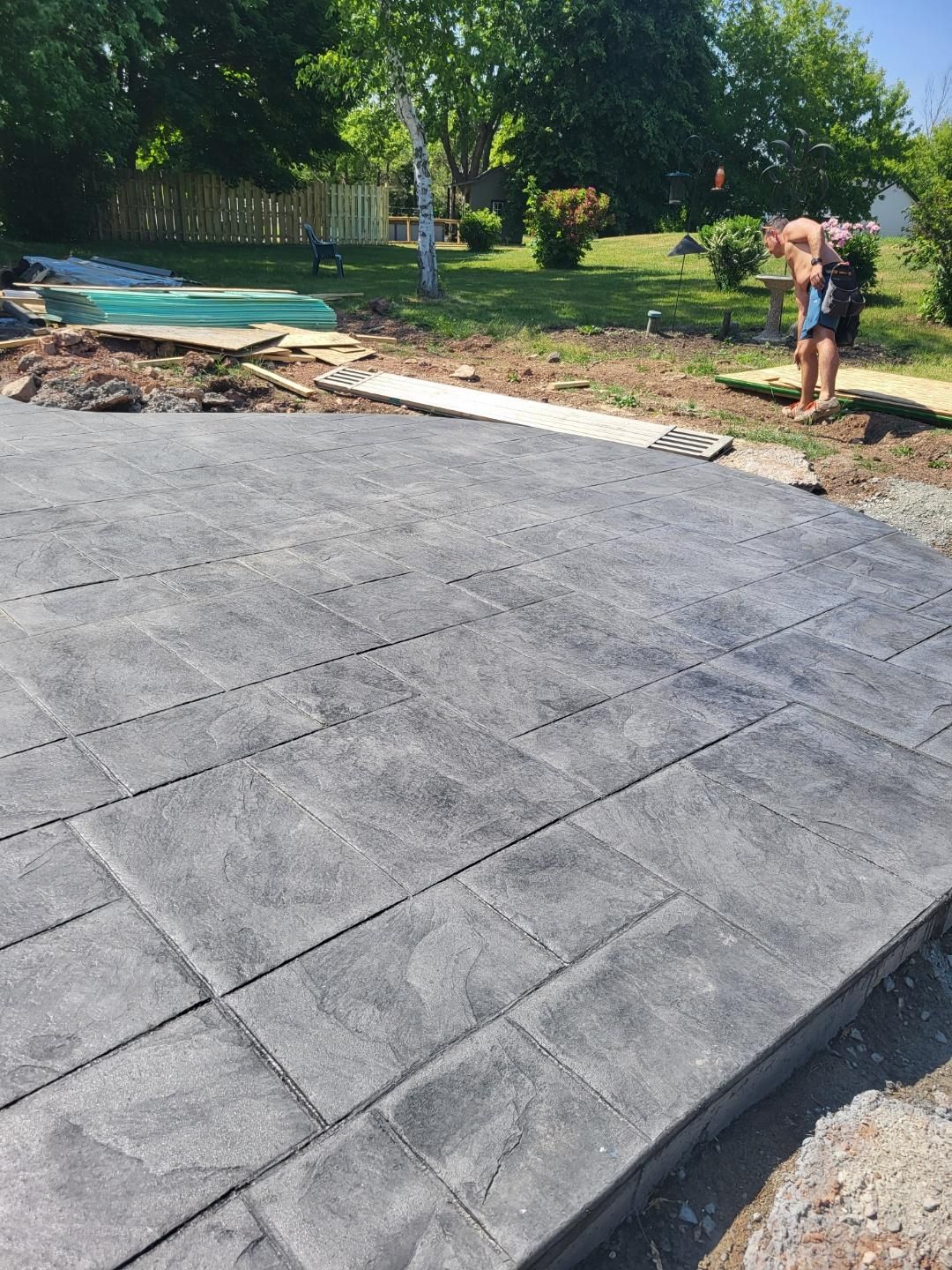 A man is standing on a concrete driveway next to a pool.