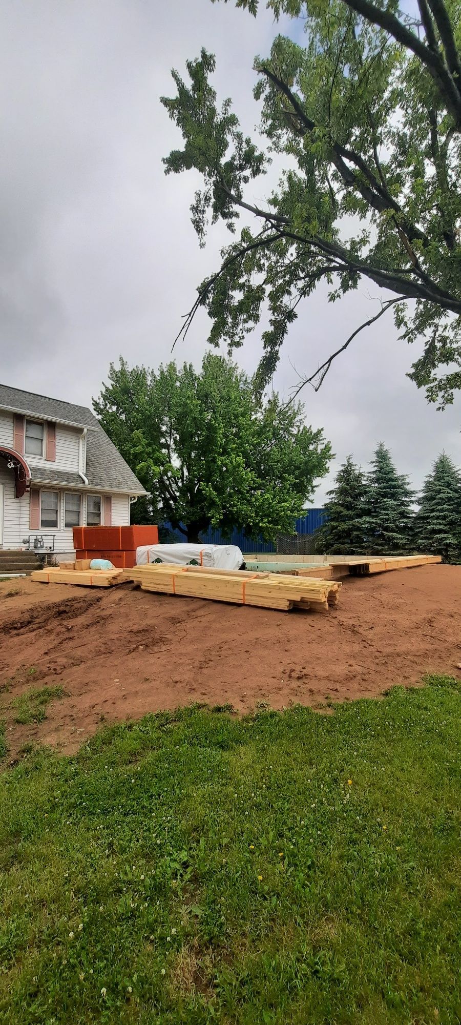 A large pile of wood is sitting in a dirt field in front of a house.