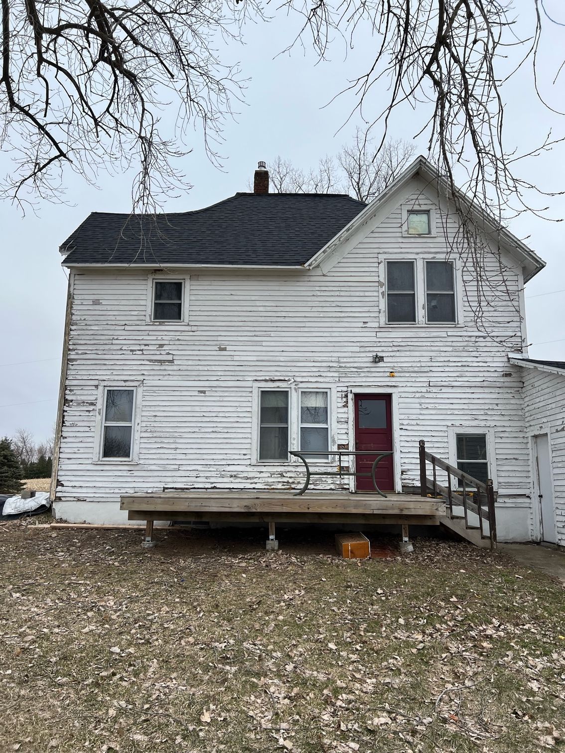 A white house with a red door and a black roof is sitting on top of a lush green field.