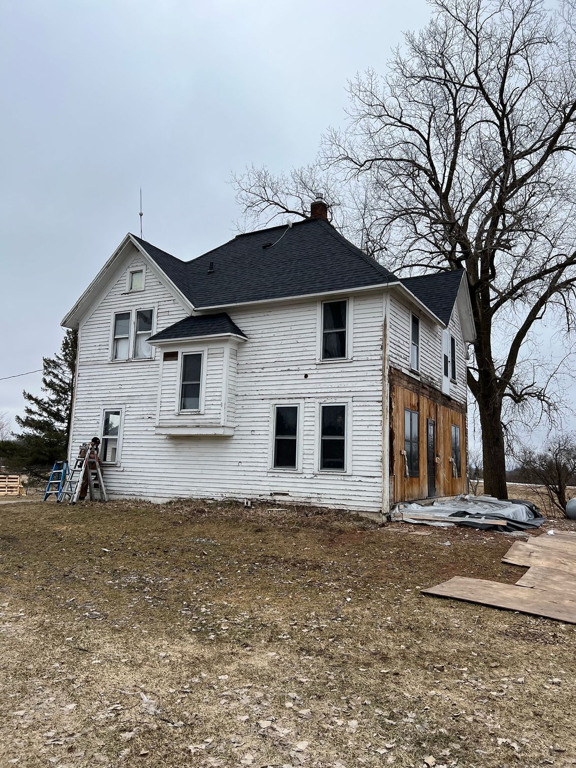 A white house with a black roof is sitting on top of a dirt field.