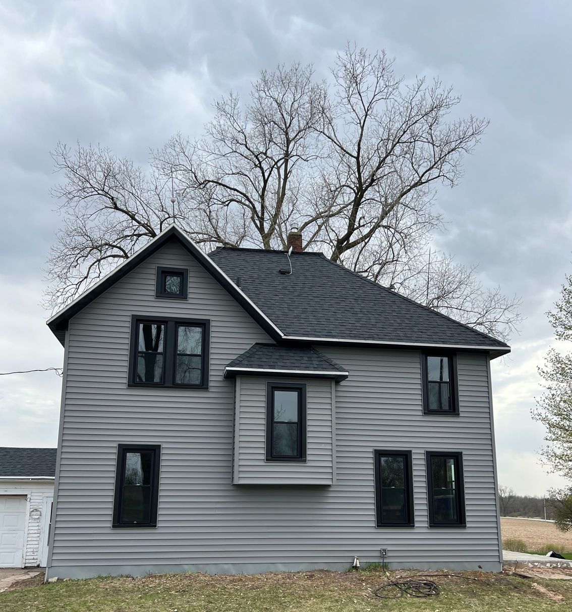 A large gray house with black windows and a tree in the background.