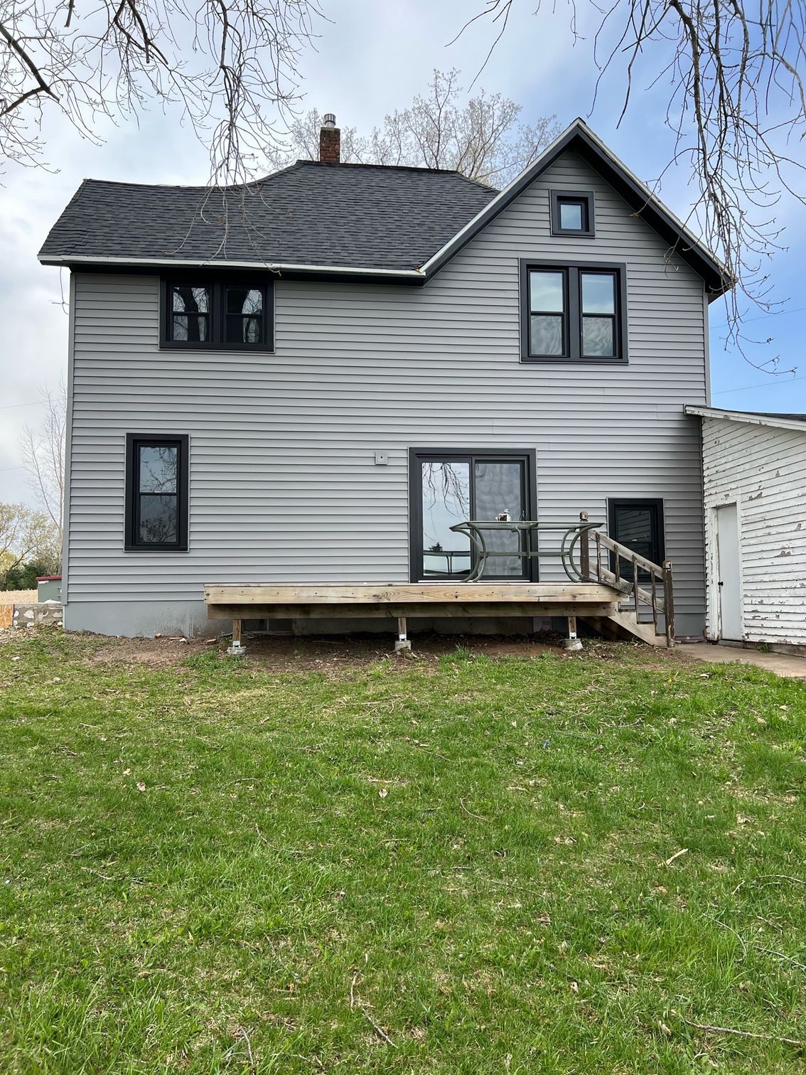 The back of a house with a deck and stairs is sitting on top of a lush green field.