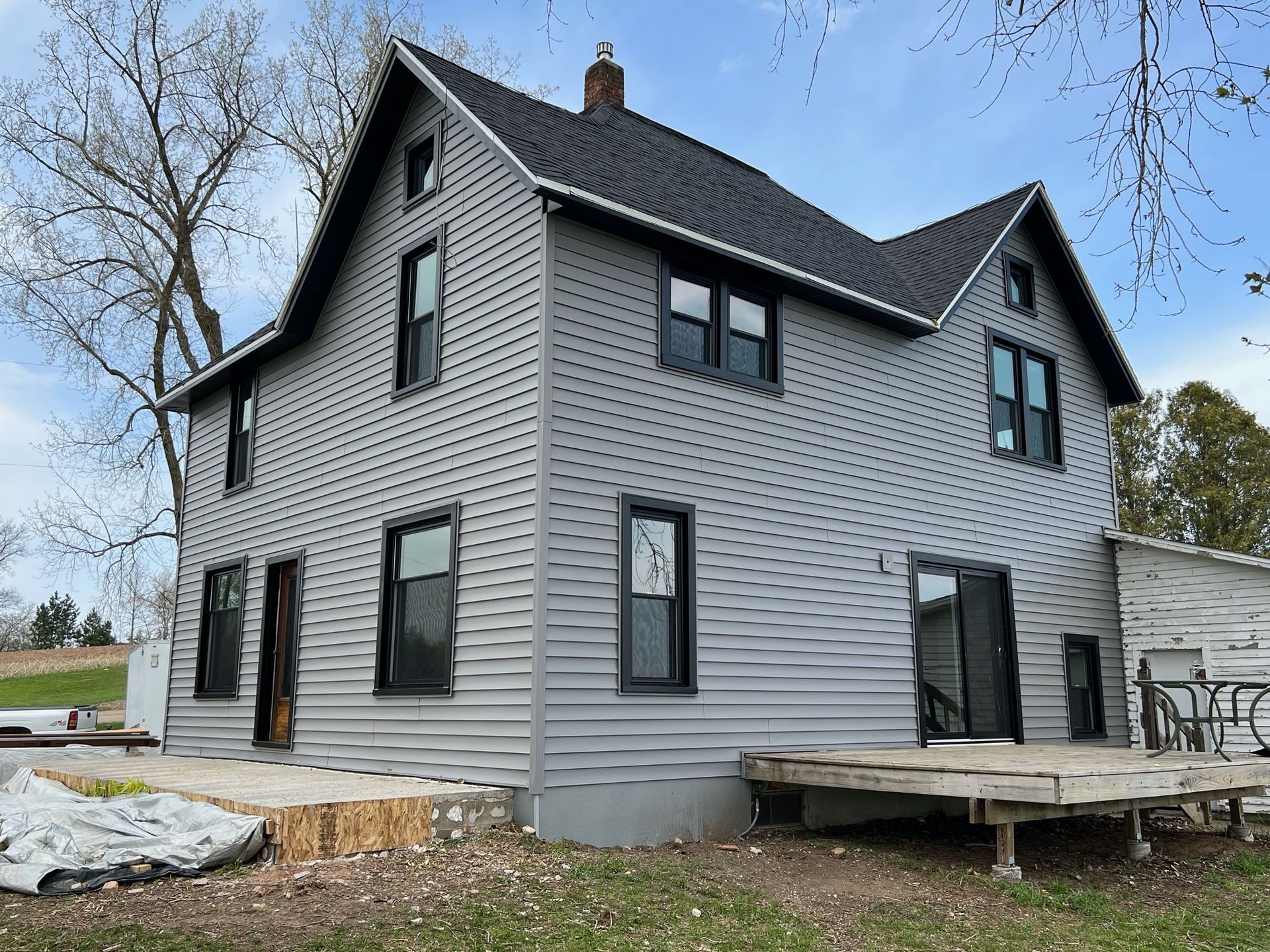 A large gray house with black windows and a black roof is sitting on top of a lush green field.