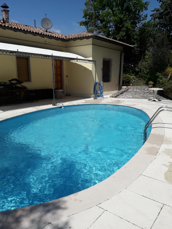Piscina ovale di fronte a una casa giallo chiaro con patio coperto.