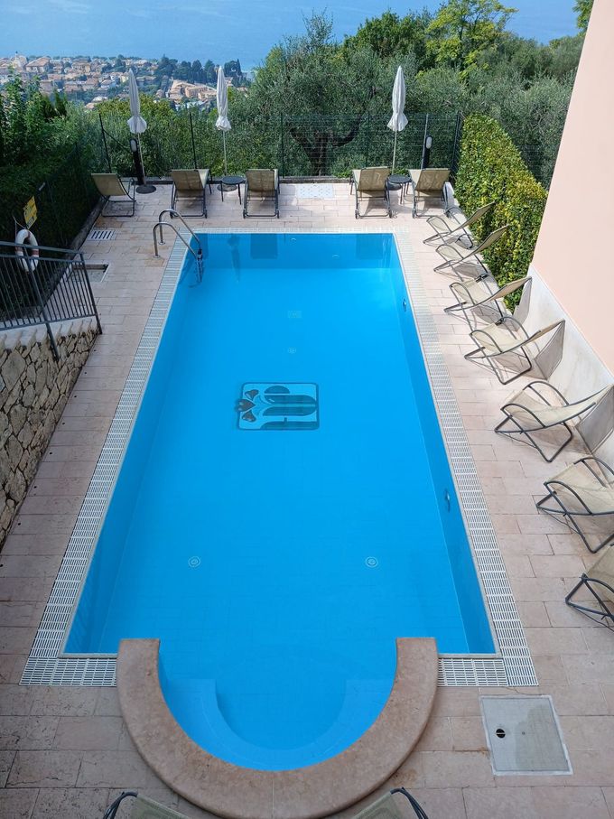 Piscina rettangolare blu con sedie a sdraio e vista sul paesaggio urbano.