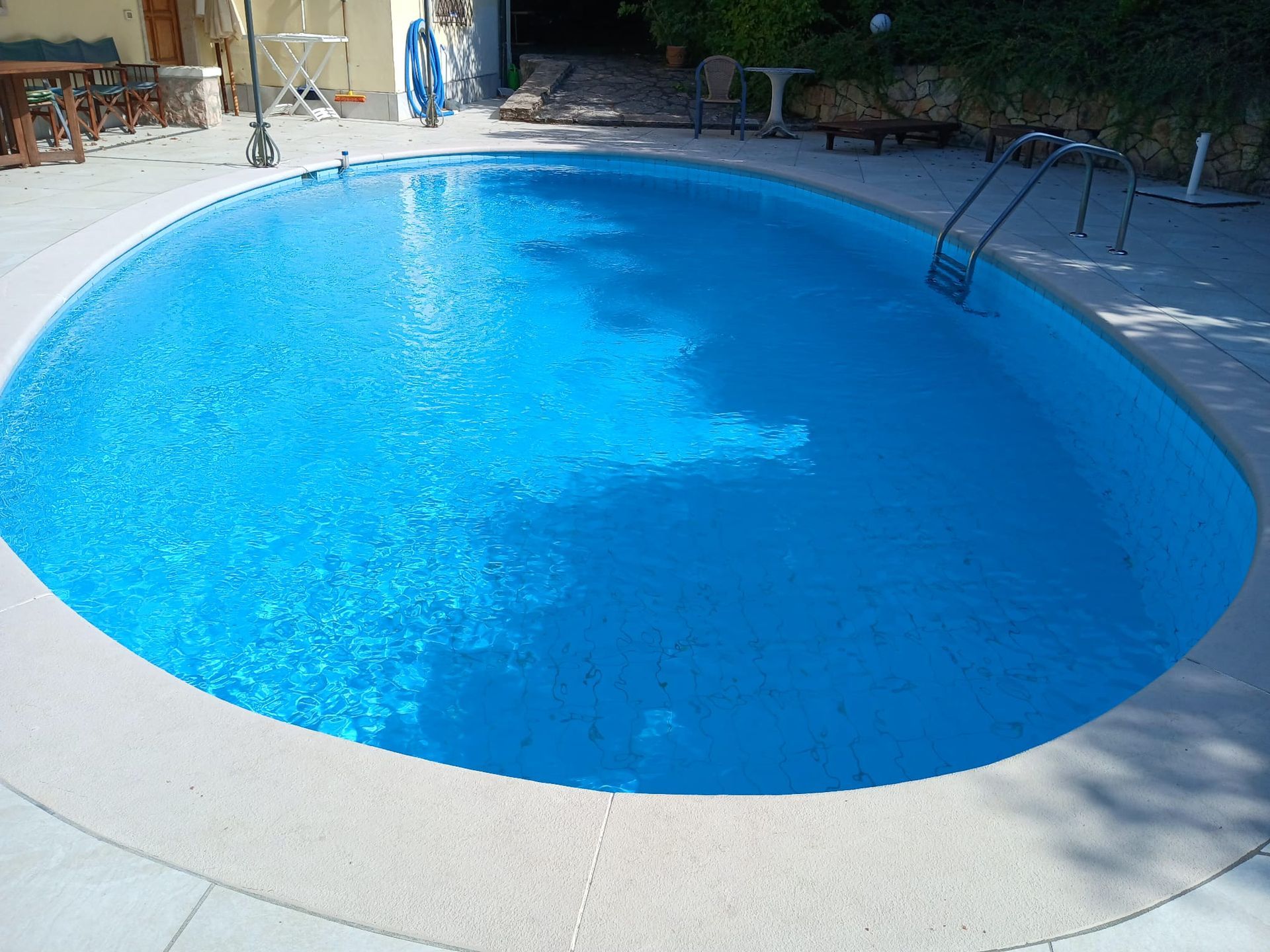 Piscina di forma ovale riempita con acqua di un azzurro brillante, circondata da un ponte in cemento di colore chiaro.