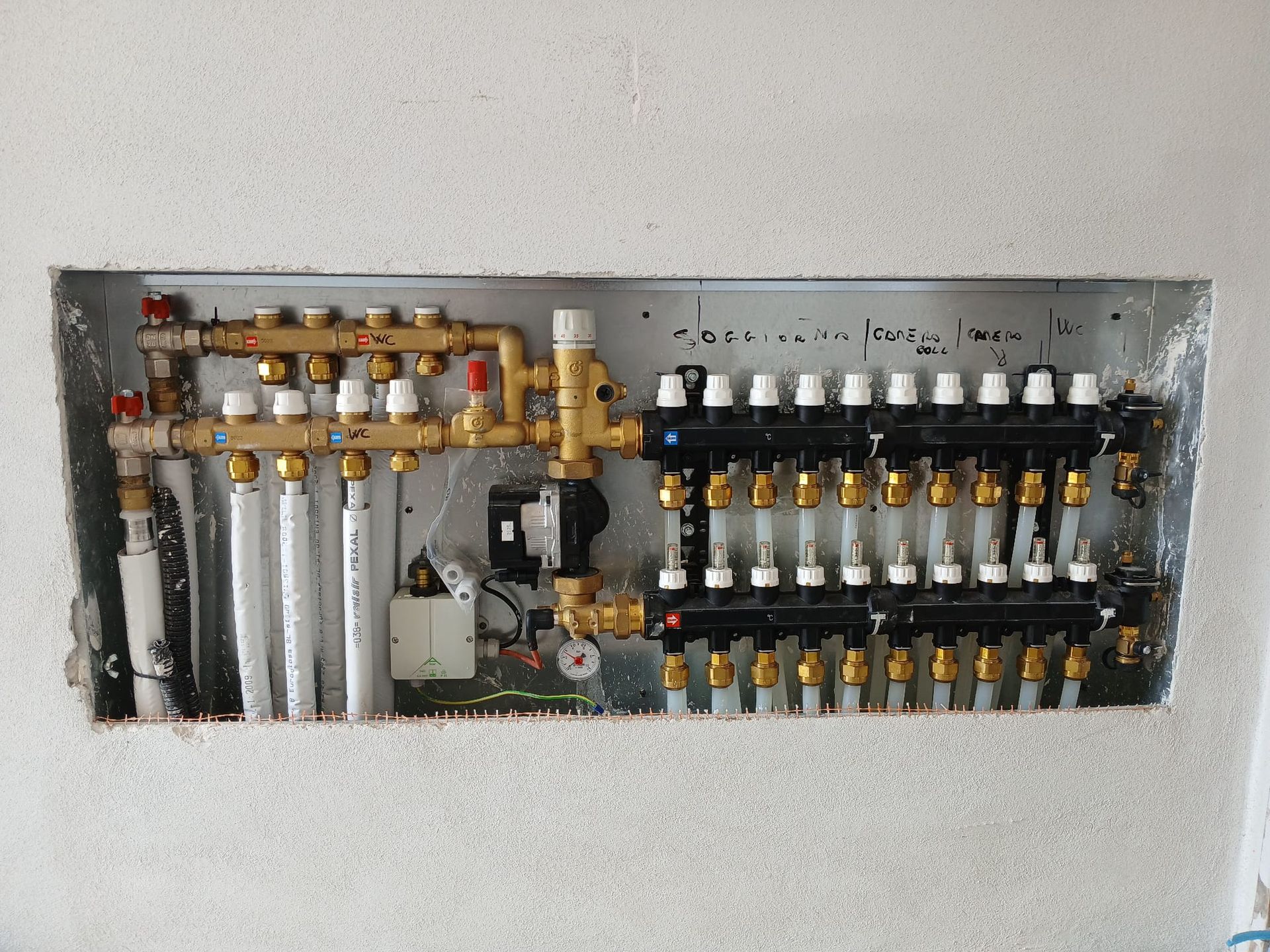 Sistema di collettori per riscaldamento a pavimento radiante, tubi, valvole e pompa installati in una cavità a parete incassata.