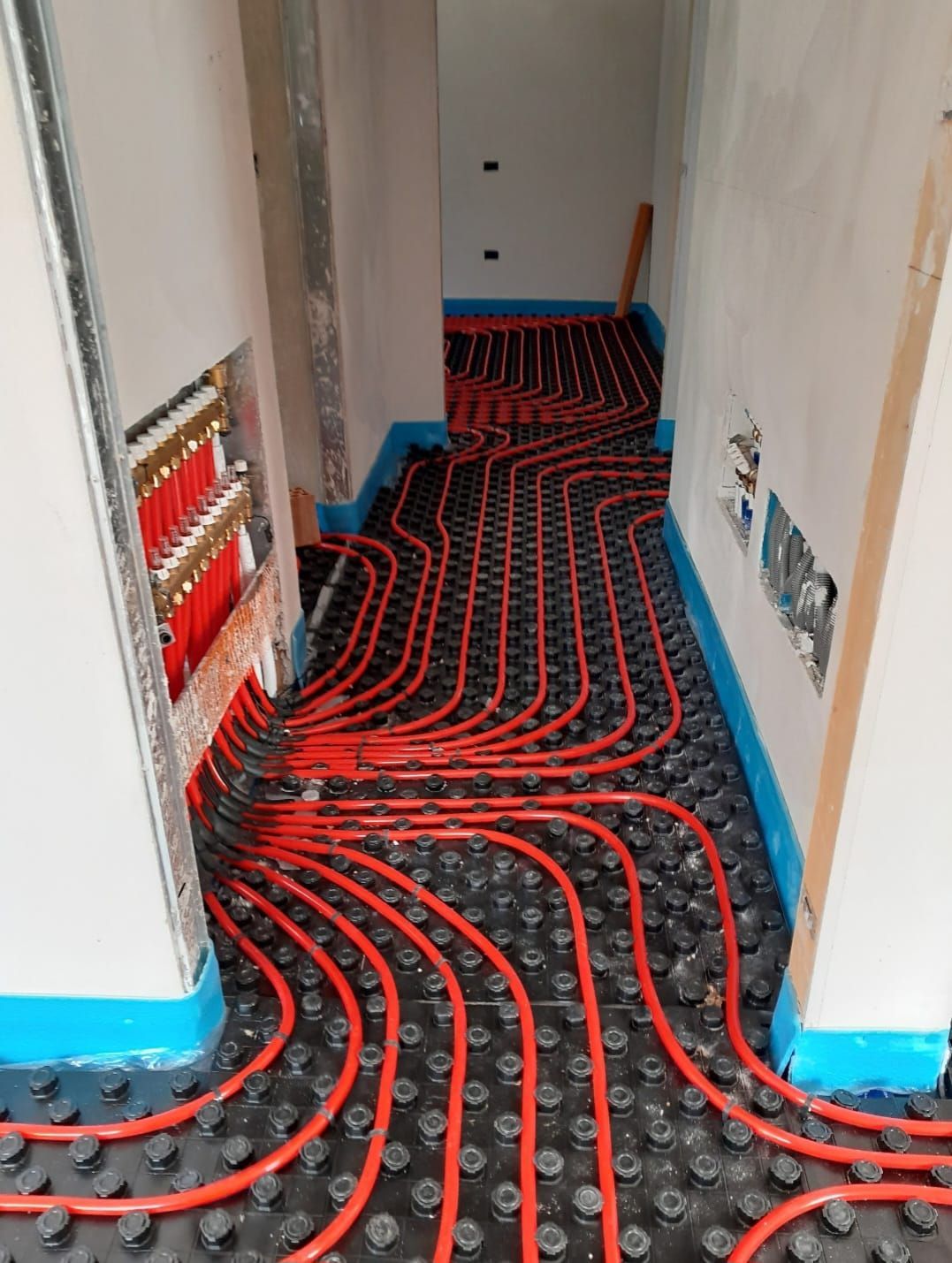 Tubi rossi di un sistema di riscaldamento a pavimento radiante in un corridoio prima dell'installazione del pavimento.