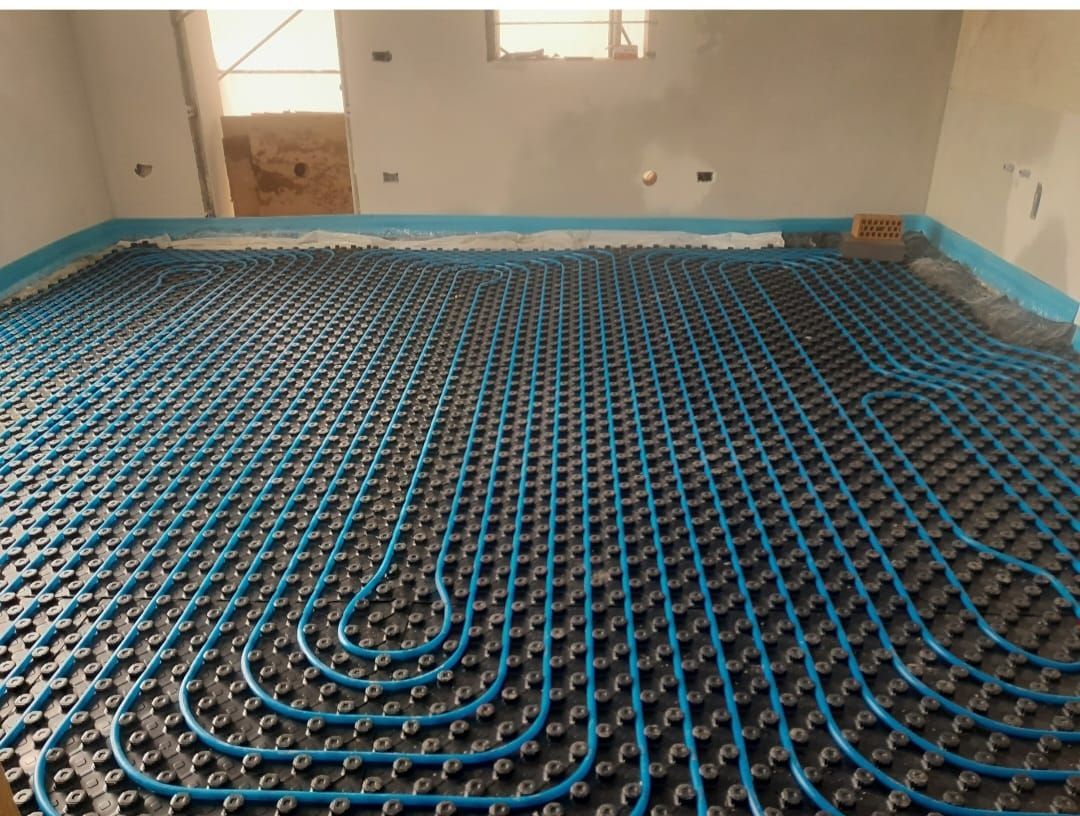 Tubi blu del riscaldamento a pavimento posati su un sottofondo scuro in una stanza in costruzione.