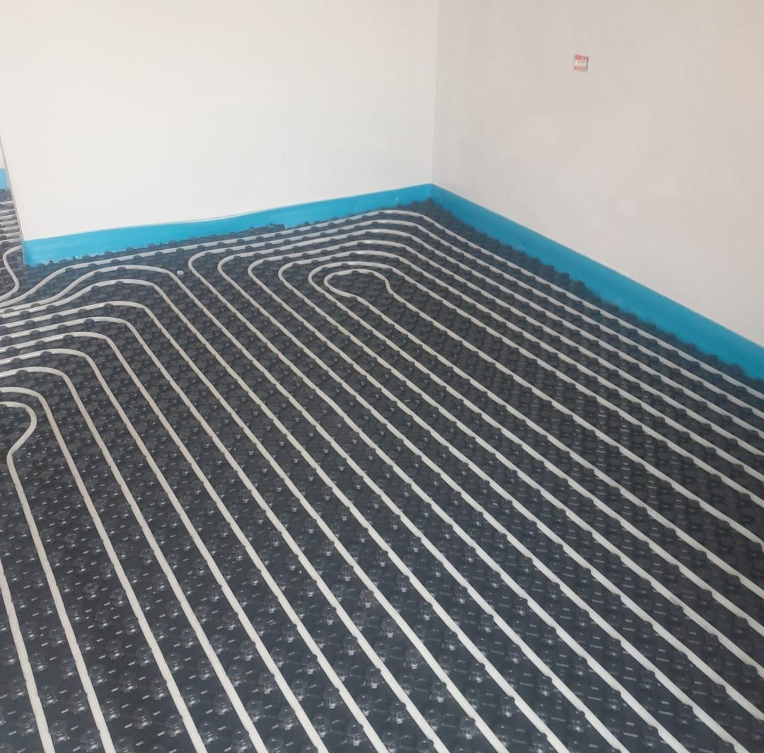 Tubi bianchi disposti in file su un tappetino nero, installati per il riscaldamento a pavimento in una stanza.