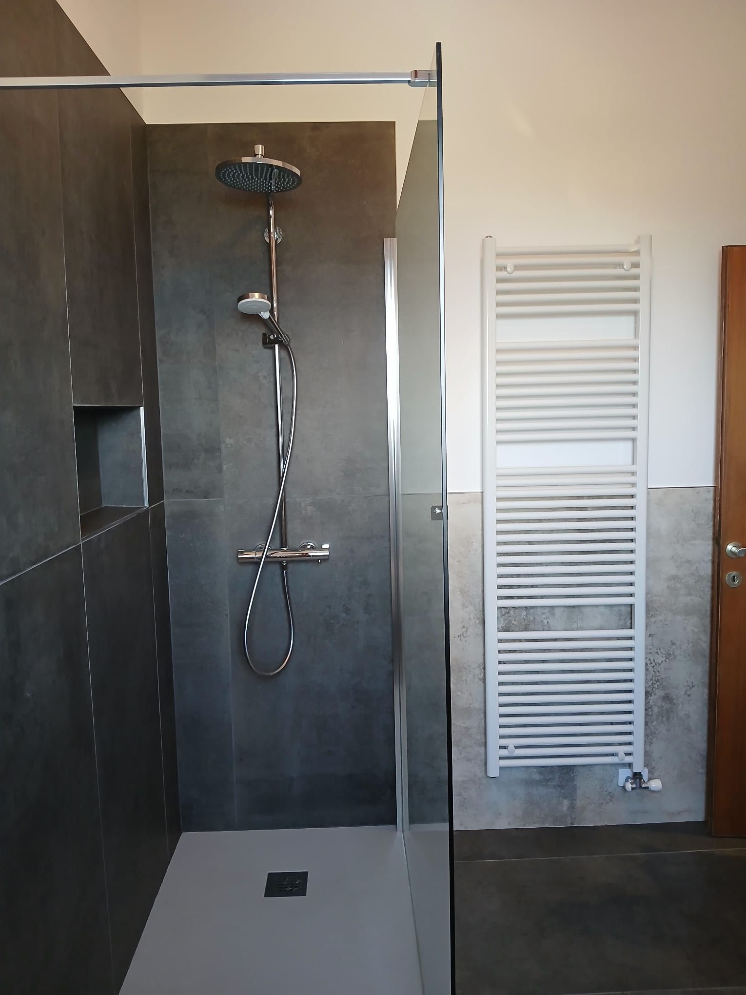 Doccia walk-in con piastrelle grigie, soffione a pioggia e scaldasalviette bianco a parete.
