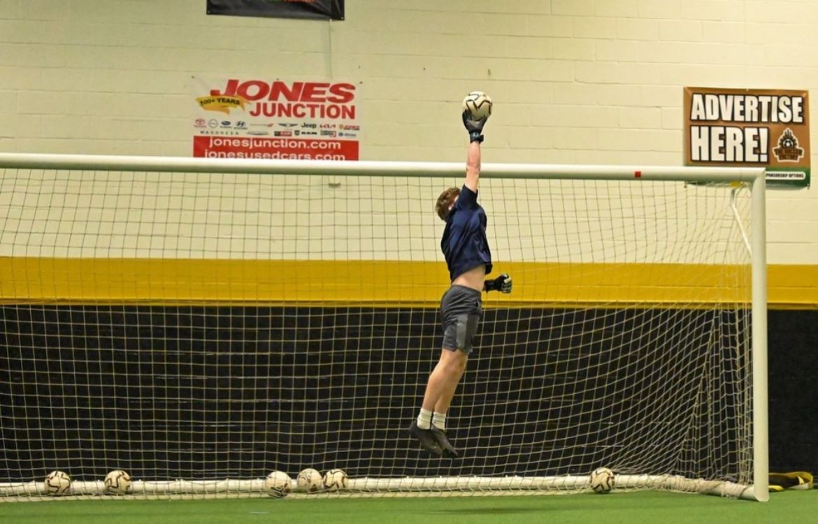 A soccer goalie is jumping in the air to catch a soccer ball.