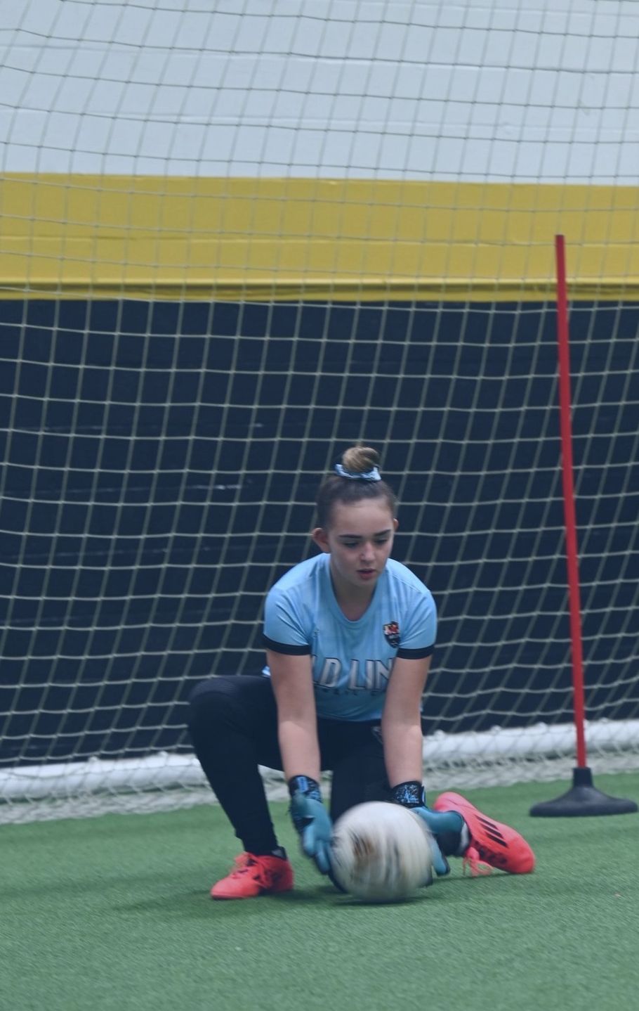 A female soccer goalie is kneeling down to catch a soccer ball
