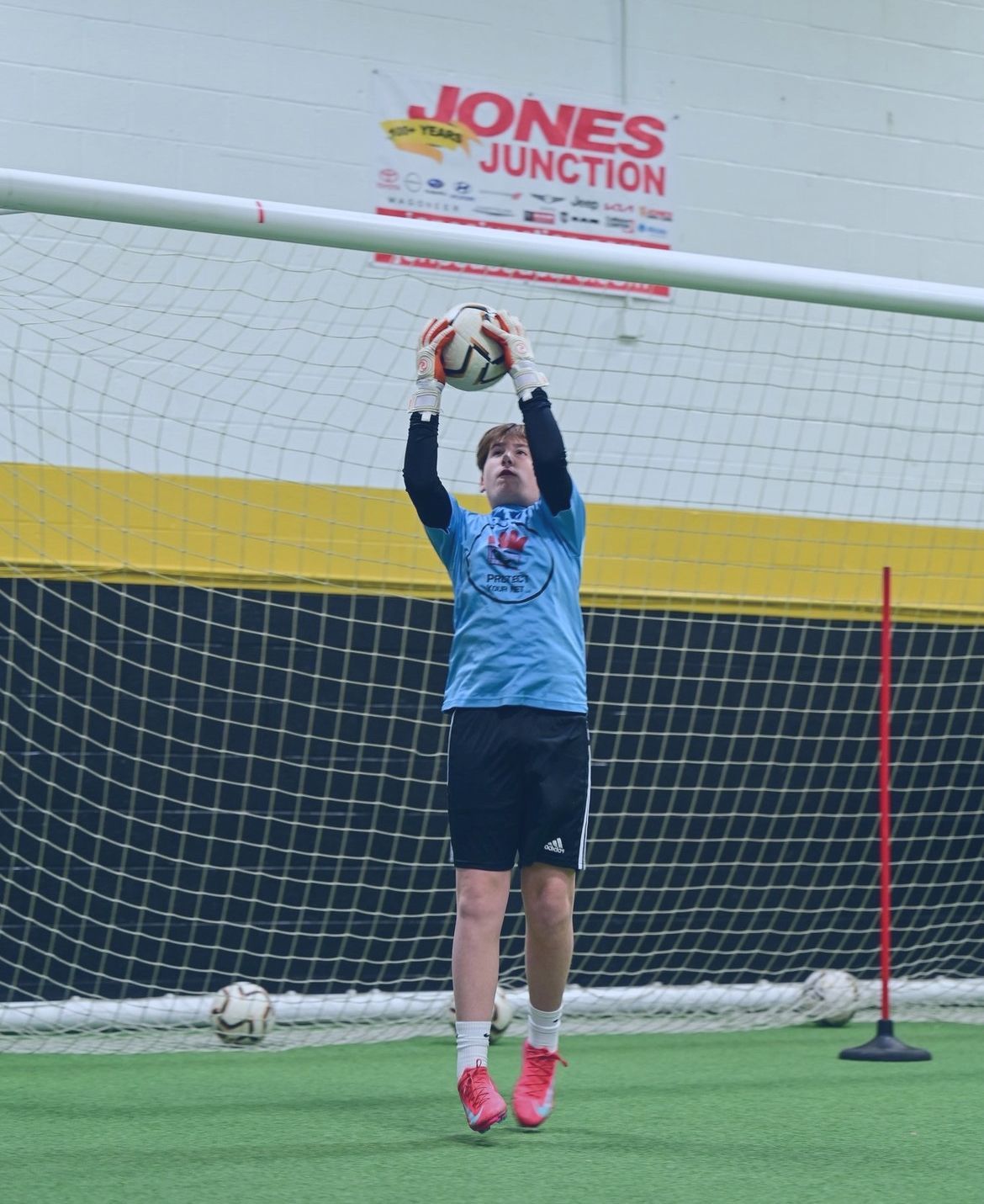 A goalie catches a soccer ball in front of a jones junction sign