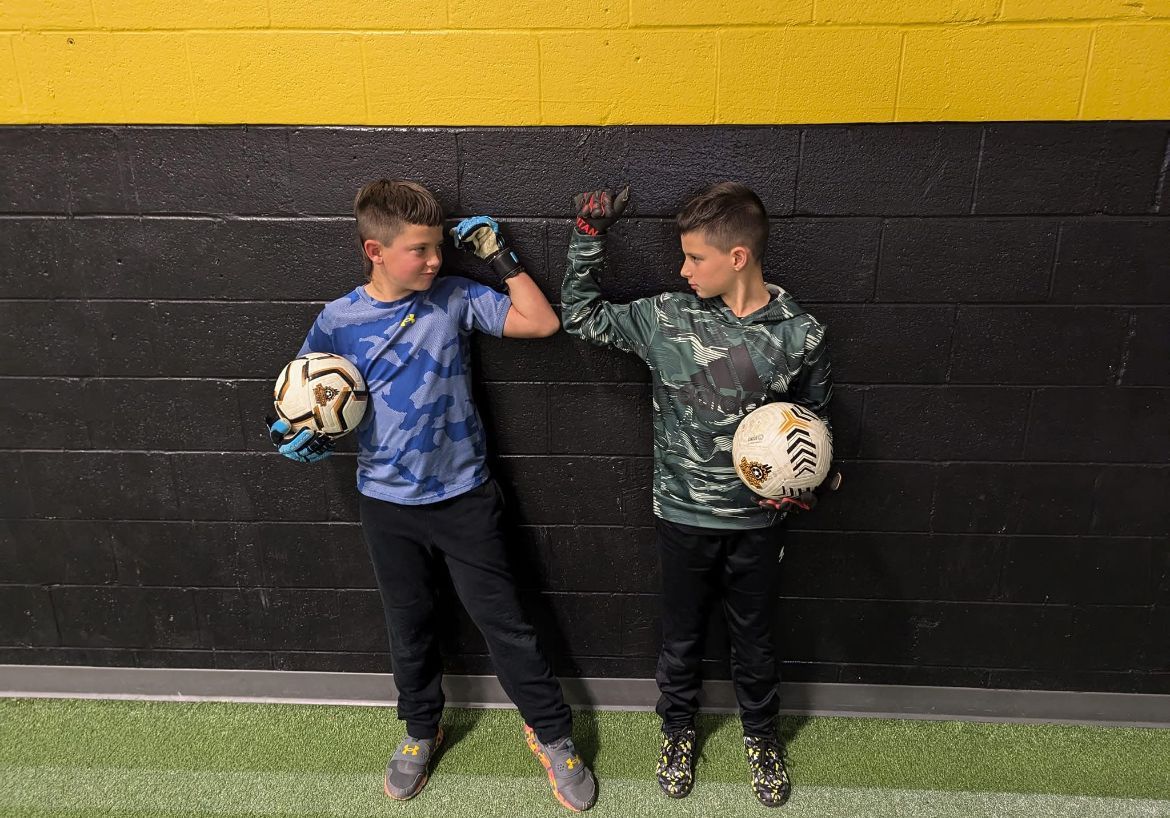 Two young boys are standing next to each other holding soccer balls.