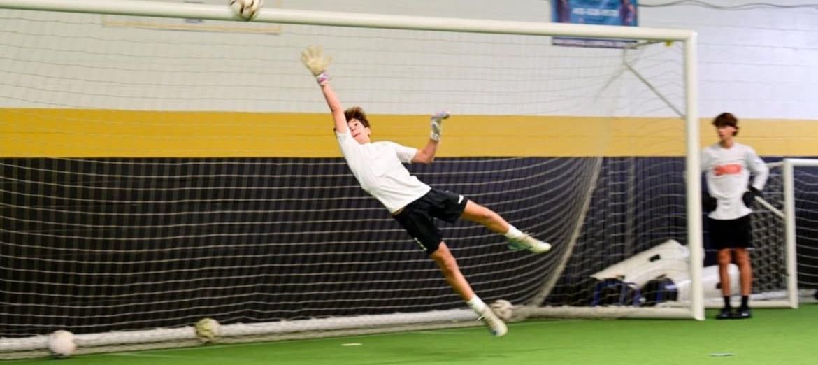 A soccer goalie is jumping in the air to catch a soccer ball.