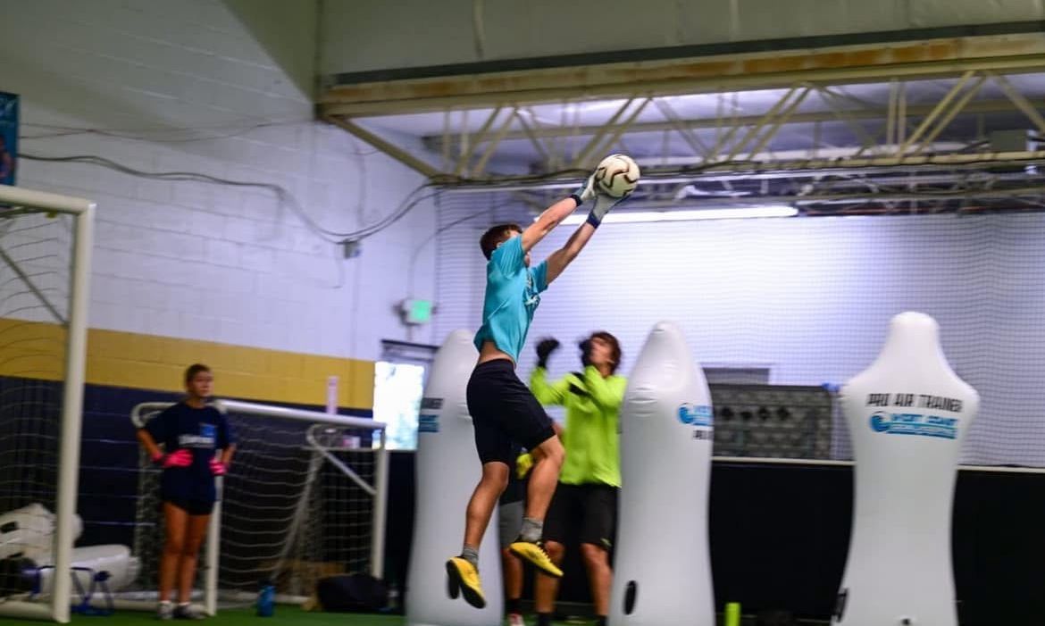 A goalie is diving to catch a soccer ball in front of a sign that says jones junction