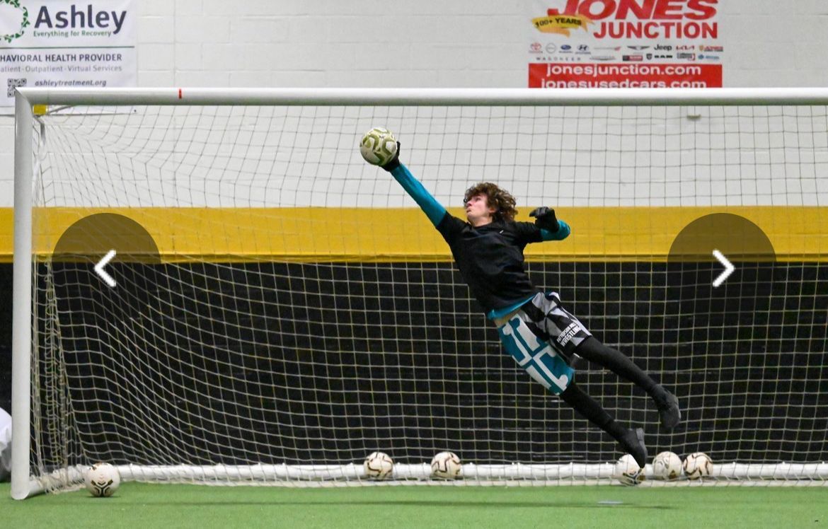 A goalie is diving to catch a soccer ball in front of a sign that says jones junction