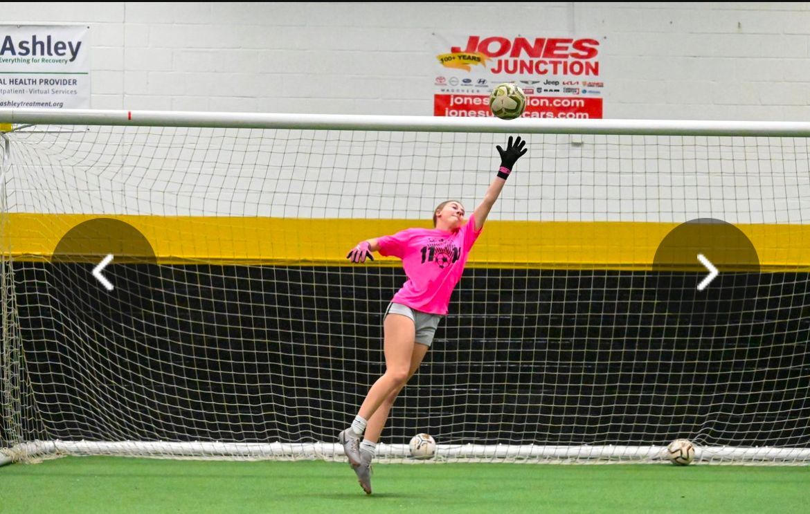 A girl in a pink shirt is jumping to catch a soccer ball