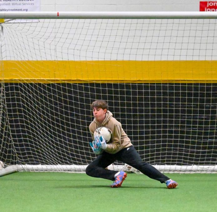 A goalie is kneeling down to catch a soccer ball