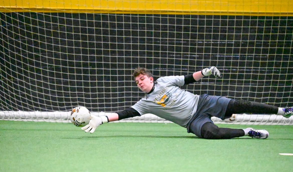 A soccer goalie is jumping in the air to catch a soccer ball.