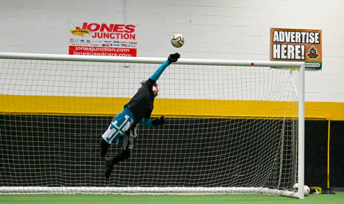 A soccer goalie is jumping in the air to catch a soccer ball.