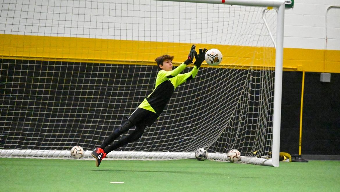 A young boy is jumping in the air to catch a soccer ball.
