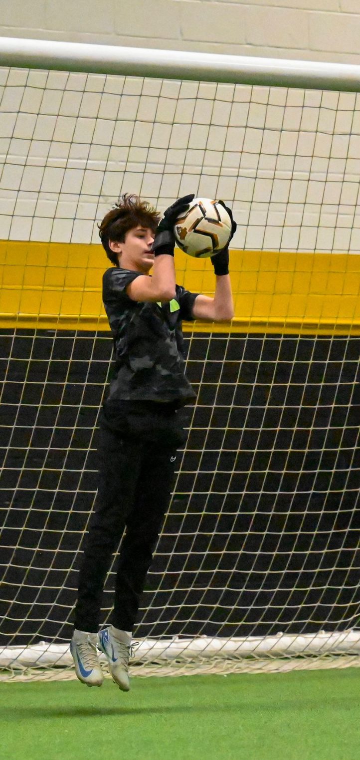 A young boy is jumping in the air to catch a soccer ball.