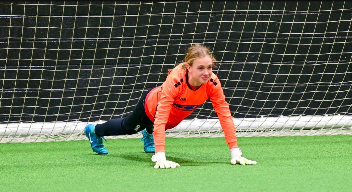 A female soccer goalie is doing push ups on the field.