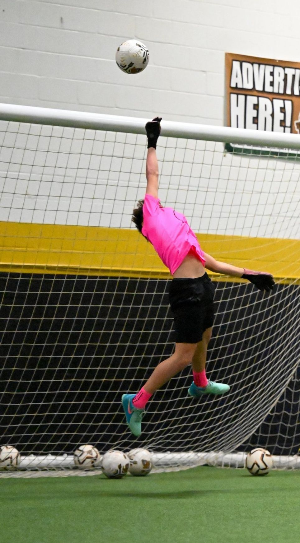 A man in a pink shirt is jumping in the air to catch a soccer ball.