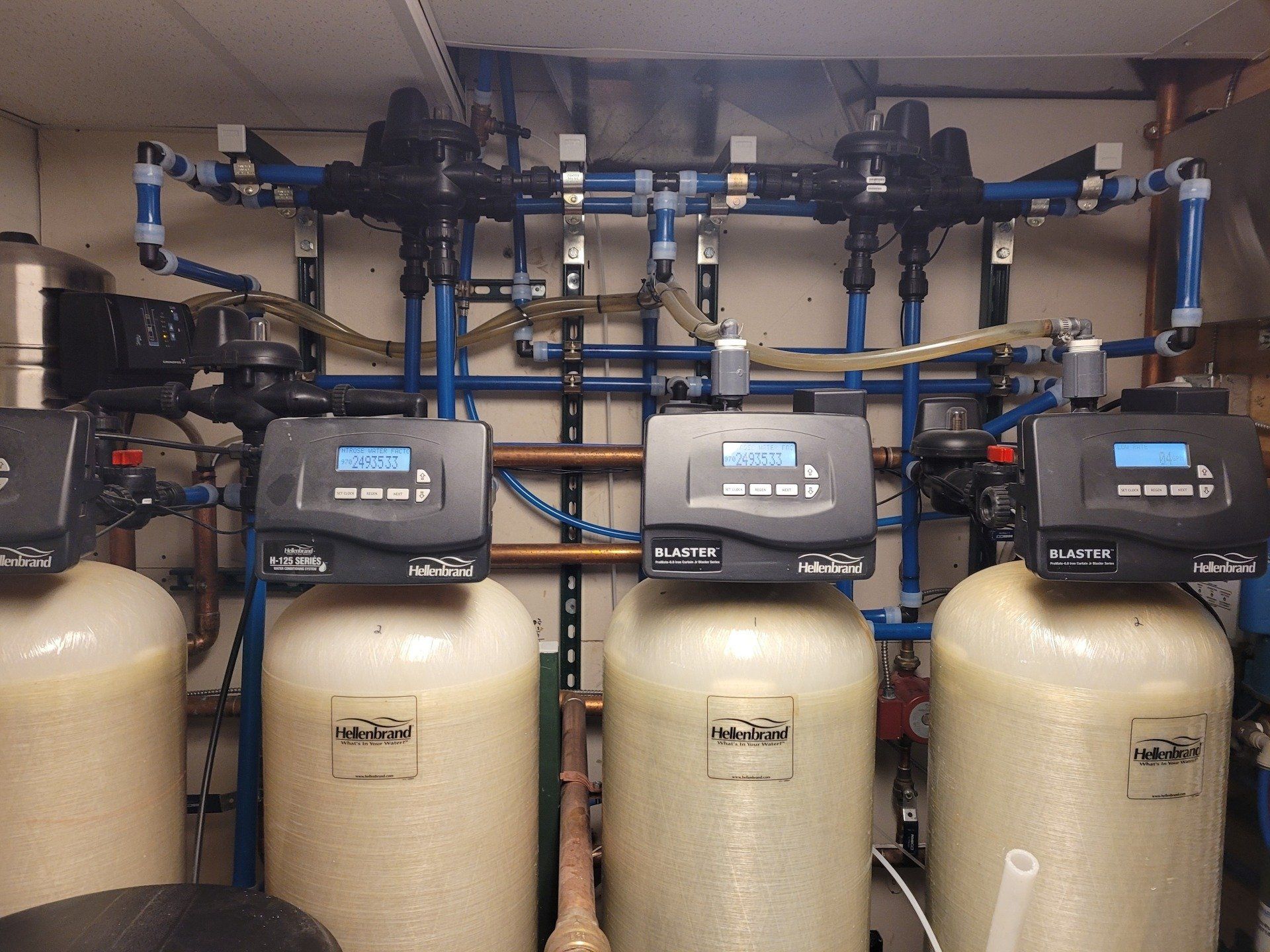 Water filtration system with multiple tanks and digital control panels, installed indoors. Blue and black pipes and tanks are visible.