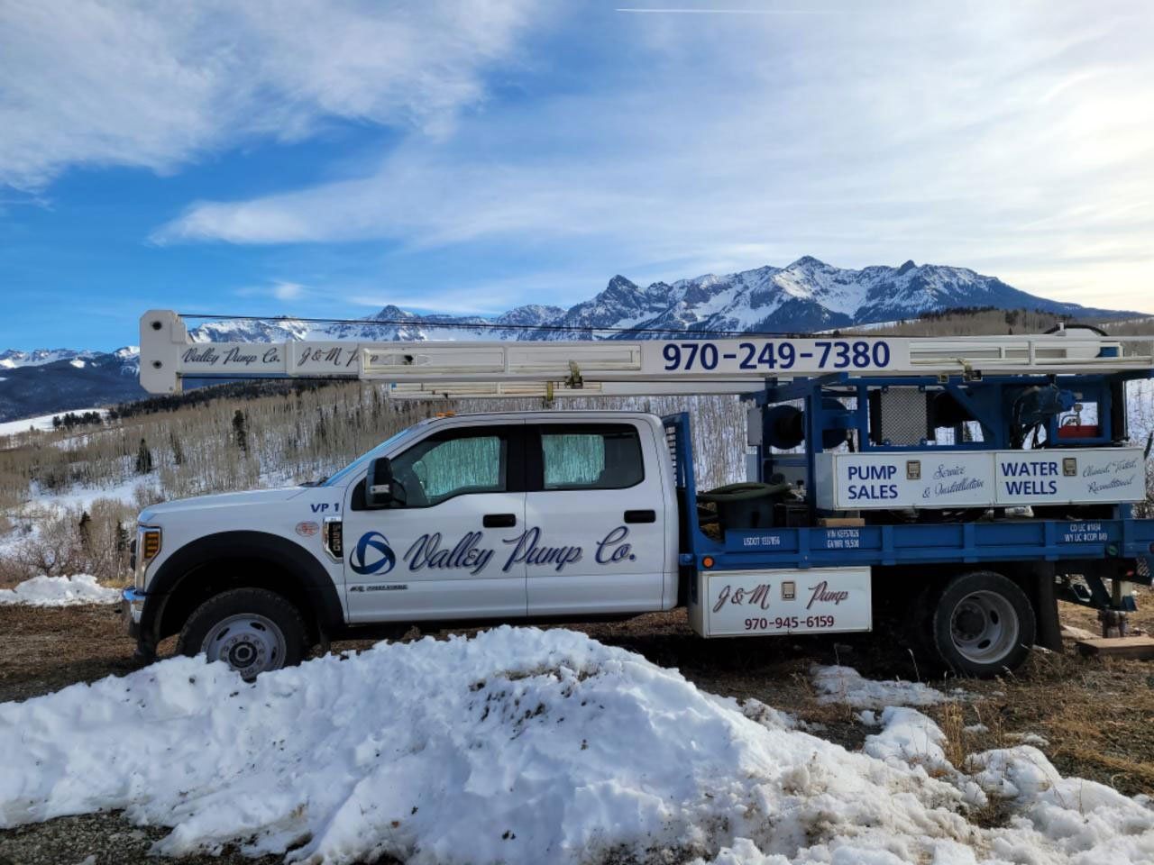 White Valley Pumps Co. truck with extended arm against snowy mountains and blue sky; phone number visible.