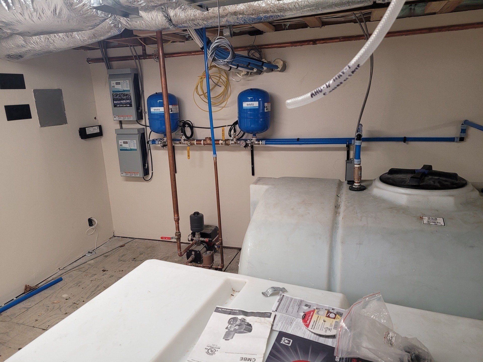 Water storage and pressure system with two blue tanks, pipes, and electrical components in a utility room. A large white tank is also present.