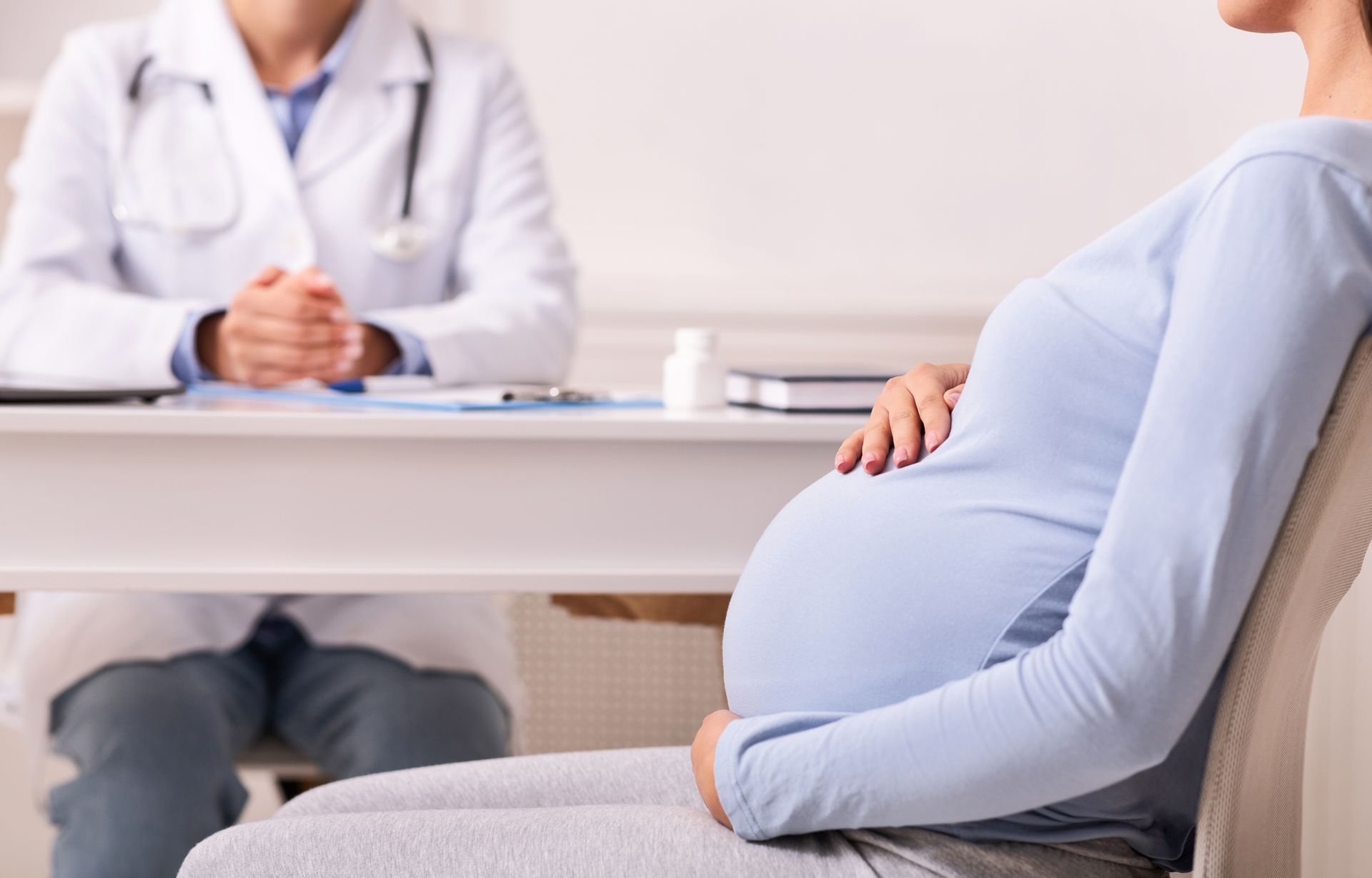 A pregnant woman is seated during a prenatal consultation with a doctor at a desk inside an office