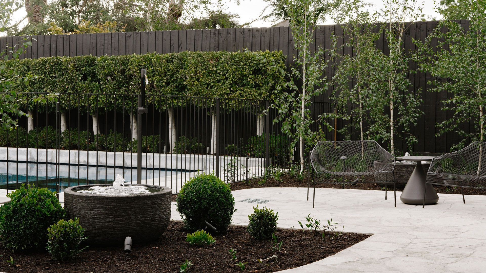Modern home with pool, lounge area, and dark wood exterior. Sunny outdoor setting.