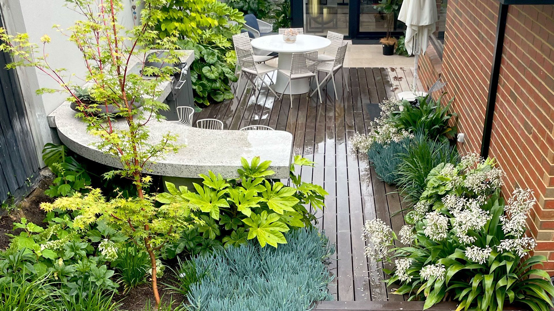 Outdoor lounge area with a pool. Features a white pergola, seating, and lush landscaping.
