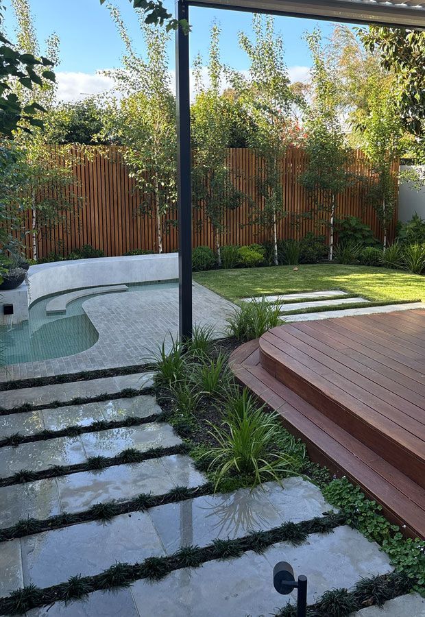 Outdoor lounge area with a pool. Features a white pergola, seating, and lush landscaping.