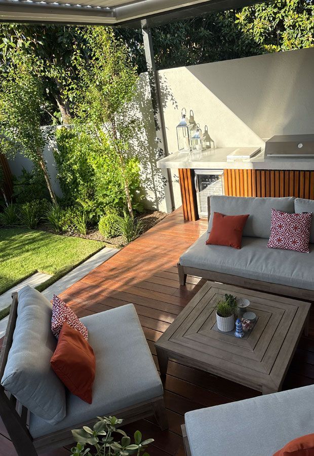 Modern house with pool, shaded patio, and wooden pergola. Turquoise water, glass walls, and dark wood siding.