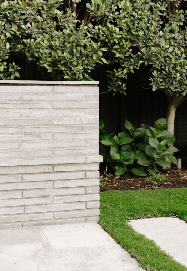 Poolside lounge area with white furniture under a wooden pergola, surrounded by lush greenery.